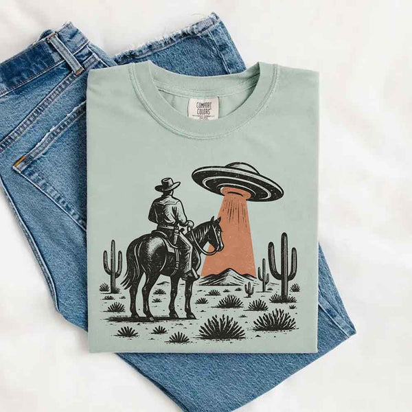 Retro cowboy and horse graphic with UFO beaming light in desert landscape with cacti – western alien mashup design