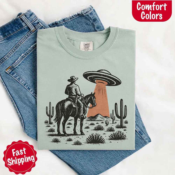 Retro cowboy and horse graphic with UFO beaming light in desert landscape with cacti – western alien mashup design
