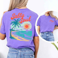 May include a short-sleeve t-shirt with “Salty Soul” printed in bold script on the front left chest and a large back graphic featuring a tropical beach scene with a palm tree, ocean waves, a bright orange sun, and flying birds.
