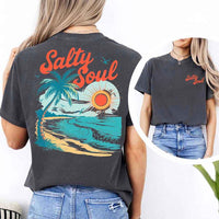 May include a short-sleeve t-shirt with “Salty Soul” printed in bold script on the front left chest and a large back graphic featuring a tropical beach scene with a palm tree, ocean waves, a bright orange sun, and flying birds.