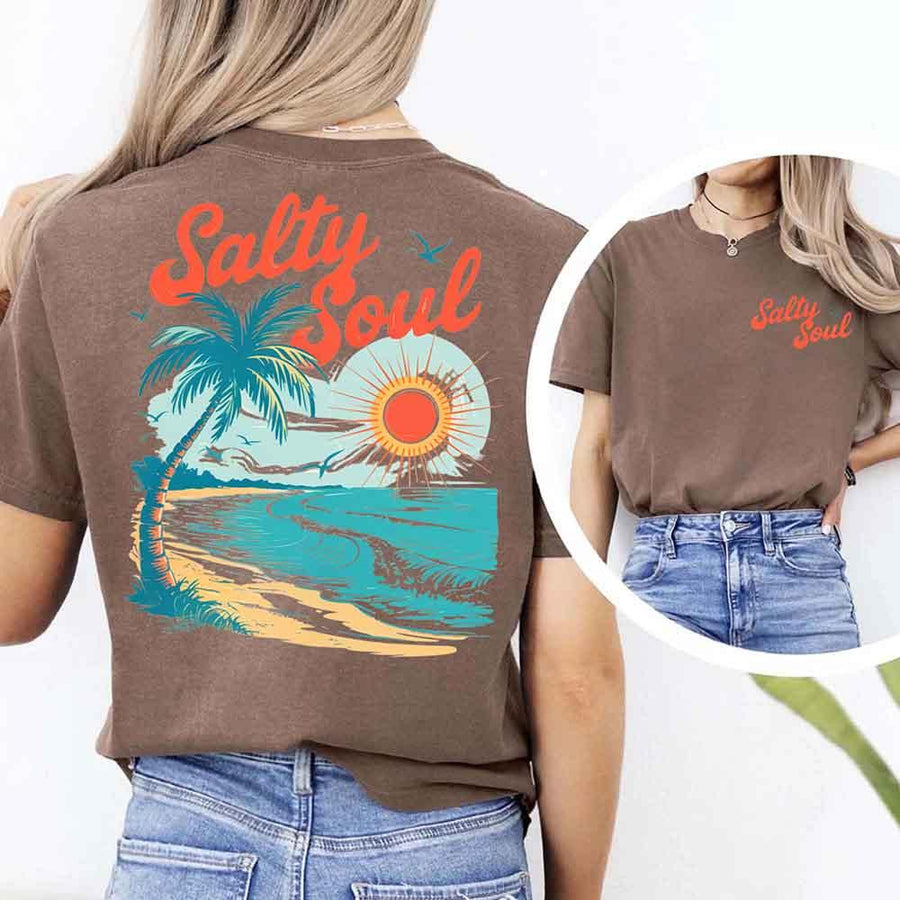 May include a short-sleeve t-shirt with “Salty Soul” printed in bold script on the front left chest and a large back graphic featuring a tropical beach scene with a palm tree, ocean waves, a bright orange sun, and flying birds.