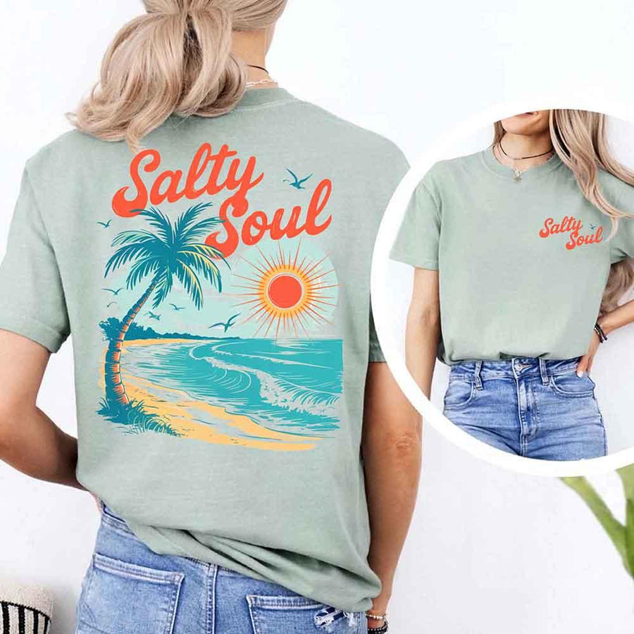 May include a short-sleeve t-shirt with “Salty Soul” printed in bold script on the front left chest and a large back graphic featuring a tropical beach scene with a palm tree, ocean waves, a bright orange sun, and flying birds.