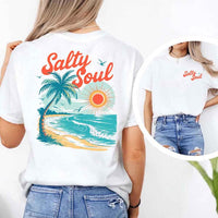 May include a short-sleeve t-shirt with “Salty Soul” printed in bold script on the front left chest and a large back graphic featuring a tropical beach scene with a palm tree, ocean waves, a bright orange sun, and flying birds.