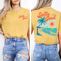 May include a short-sleeve t-shirt with “Salty Soul” printed in bold script on the front left chest and a large back graphic featuring a tropical beach scene with a palm tree, ocean waves, a bright orange sun, and flying birds.