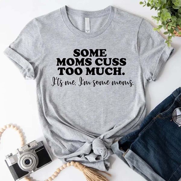 Gray t-shirt with humorous text some moms cuss too much on a white surface with accessories.