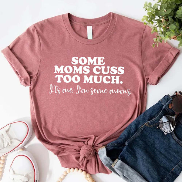 Mauve t-shirt with humorous text some mom cuss too much on a white surface with jeans and sneakers.