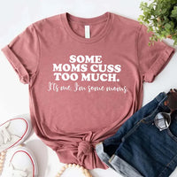 Mauve t-shirt with humorous text some mom cuss too much on a white surface with jeans and sneakers.