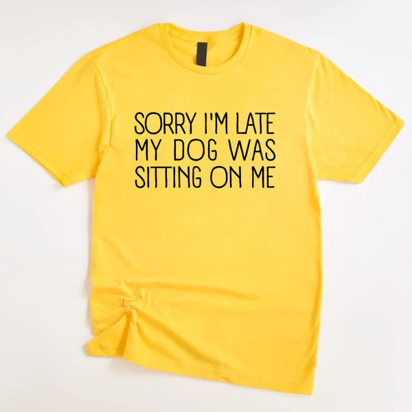 t-shirt with 'Sorry I'm late my dog was sitting on me' text, paired with jeans and sneakers on a wooden surface.