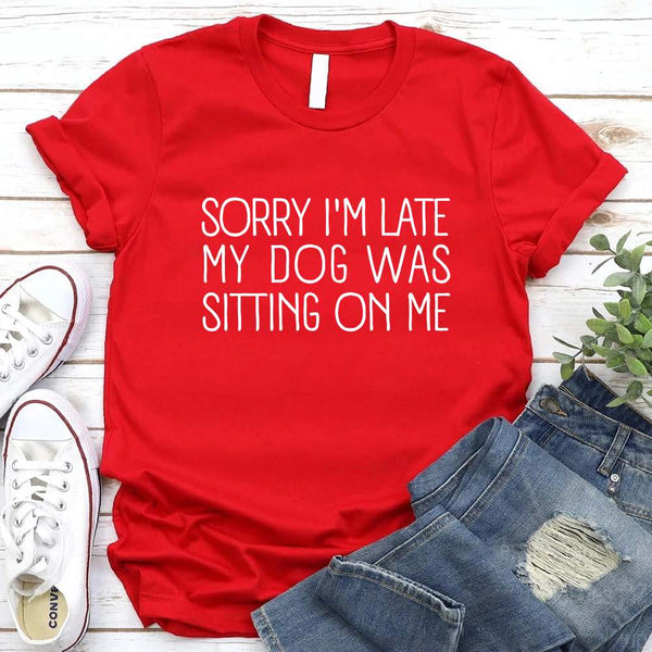 t-shirt with 'Sorry I'm late my dog was sitting on me' text, paired with jeans and sneakers on a wooden surface.