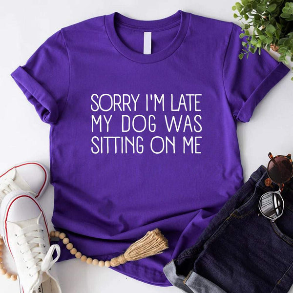 t-shirt with 'Sorry I'm late my dog was sitting on me' text, paired with jeans and sneakers on a wooden surface.