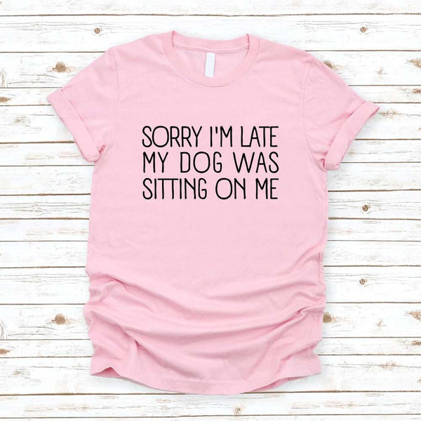 Pink t-shirt with text 'Sorry I'm late my dog was sitting on me' on a wooden surface