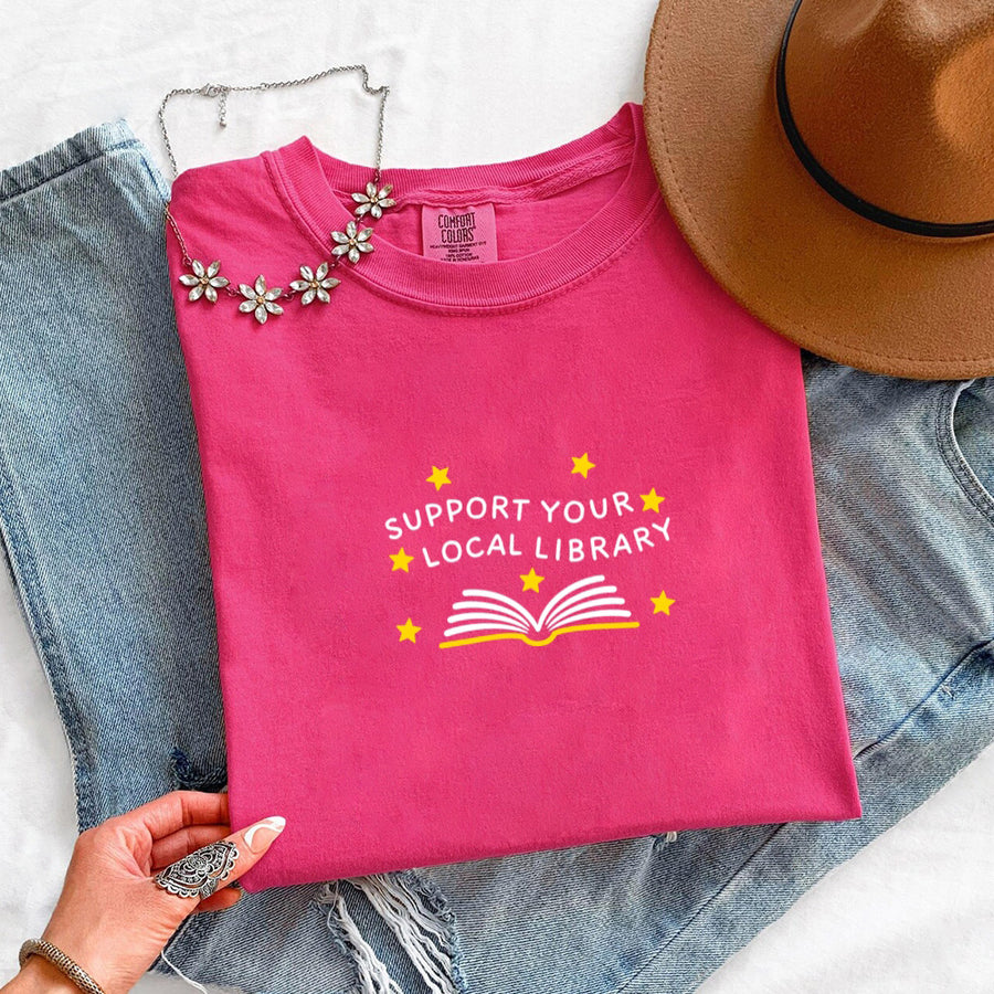 May include a Support Your Local Library Comfort Colors T-Shirt featuring a simple library-inspired statement design.