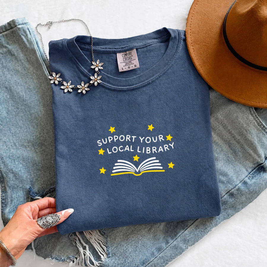 May include a Support Your Local Library Comfort Colors T-Shirt featuring a simple library-inspired statement design.