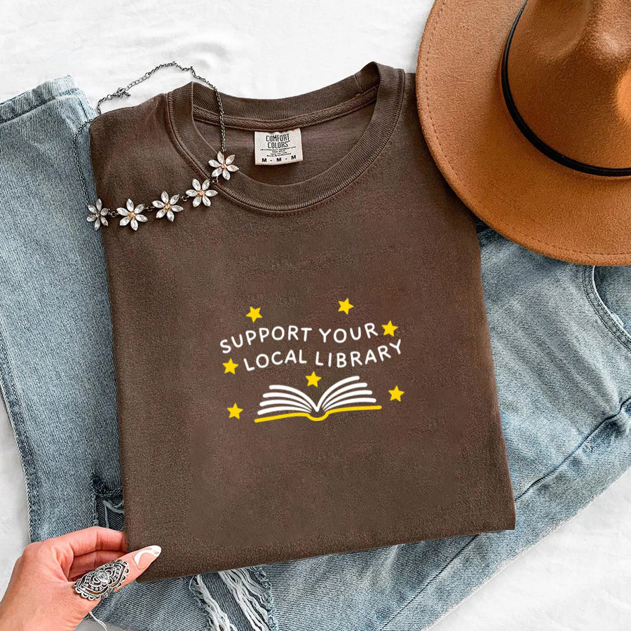 May include a Support Your Local Library Comfort Colors T-Shirt featuring a simple library-inspired statement design.