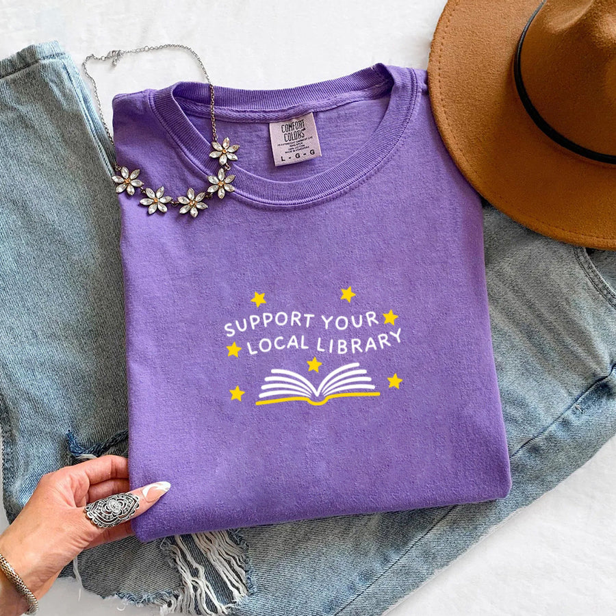 May include a Support Your Local Library Comfort Colors T-Shirt featuring a simple library-inspired statement design.