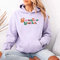 Person wearing a lavender hoodie with 'Sweater Weather' text, sitting on a white surface.