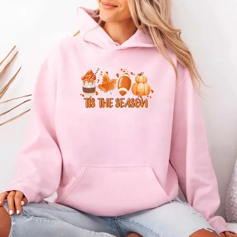 Person wearing a pink hoodie with 'Tis the Season' text and autumn graphics.