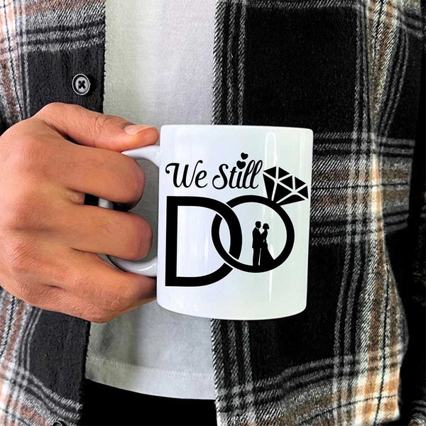 Person holding a mug with 'We Still Do' design, wearing a plaid shirt.