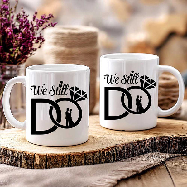 Two white mugs with 'We Still Do' design on a wooden surface.
