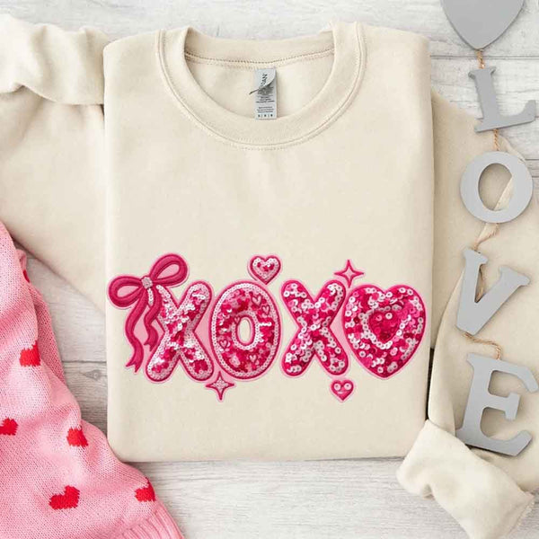 May include a crewneck sweatshirt featuring an XOXO design with a faux printed sequin appearance on the front.