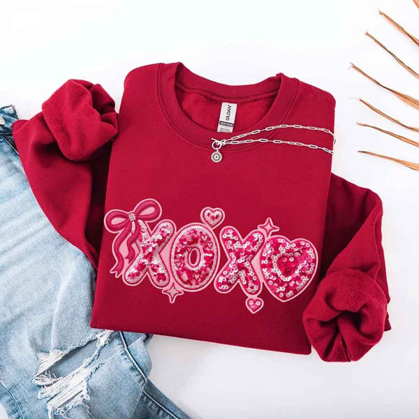 May include a crewneck sweatshirt featuring an XOXO design with a faux printed sequin appearance on the front.