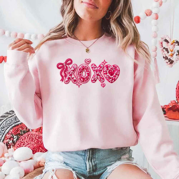 May include a crewneck sweatshirt featuring an XOXO design with a faux printed sequin appearance on the front.