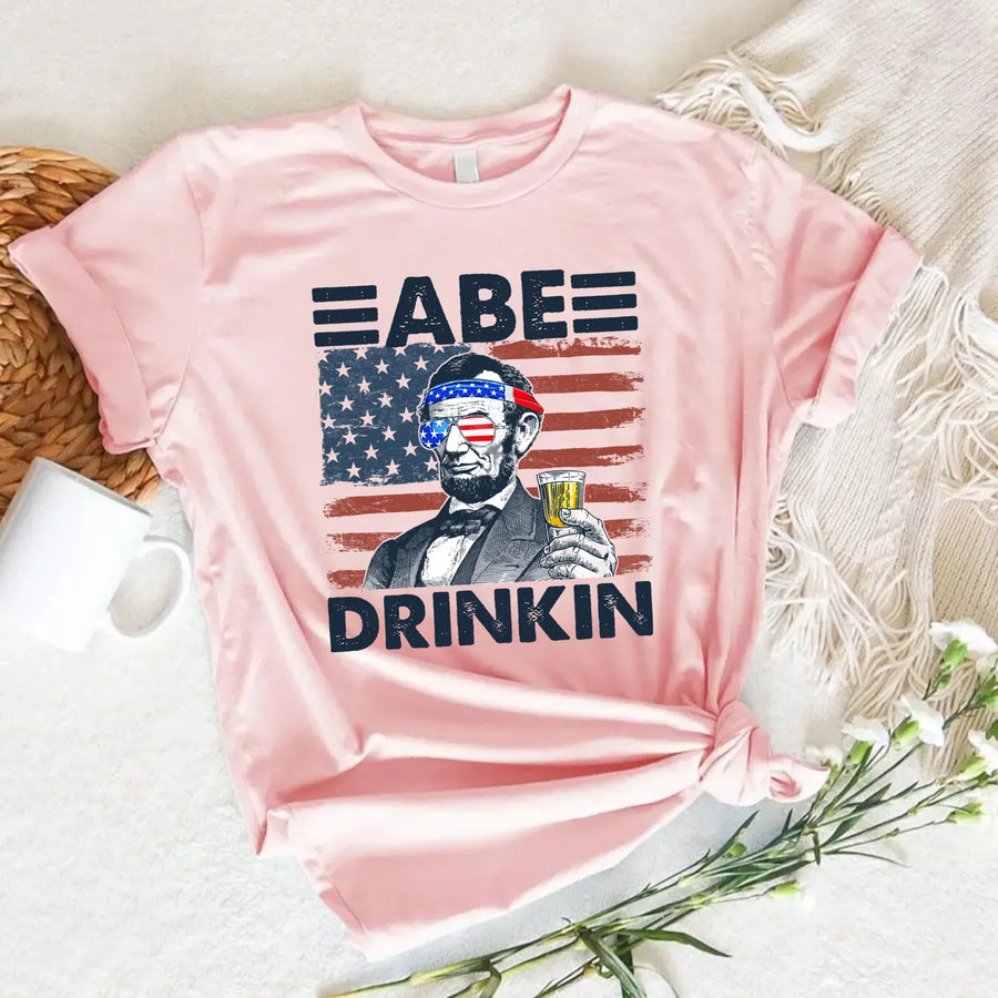 Pink 4th of July t-shirt with Abraham Lincoln, American flag sunglasses, and a drink