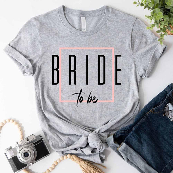 Gray t-shirt with 'BRIDE to be' text on a white surface with accessories.