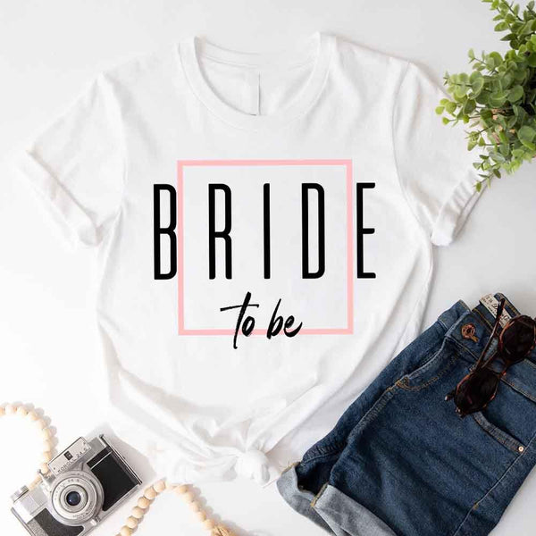 White t-shirt with 'Bride to be' text on a white surface with denim shorts and sunglasses.