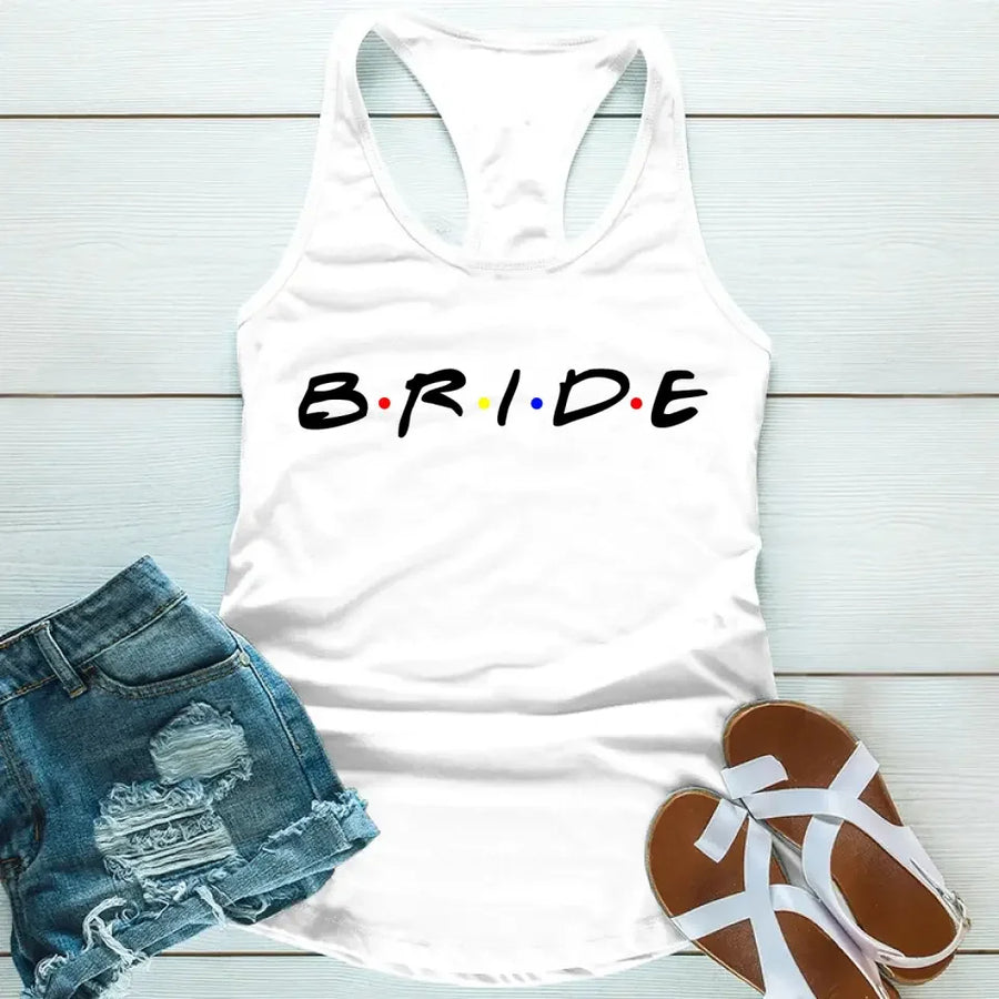 White tank top with the word 'BRIDE' printed in black letters, positioned on a wooden surface with blue denim shorts and white sandals in the background.