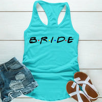 sky blue tank top with the word 'BRIDE' printed in black letters, positioned on a wooden surface with blue denim shorts and white sandals in the background.