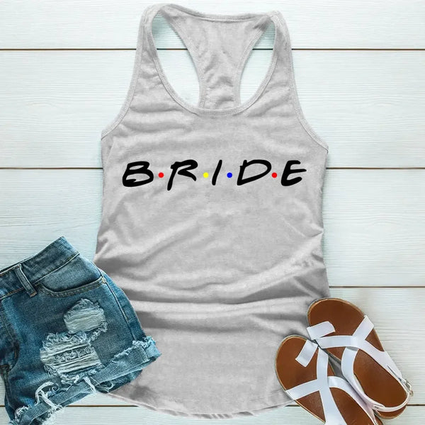 Grey tank top with the word 'BRIDE' printed in black letters, positioned on a wooden surface with blue denim shorts and white sandals in the background.