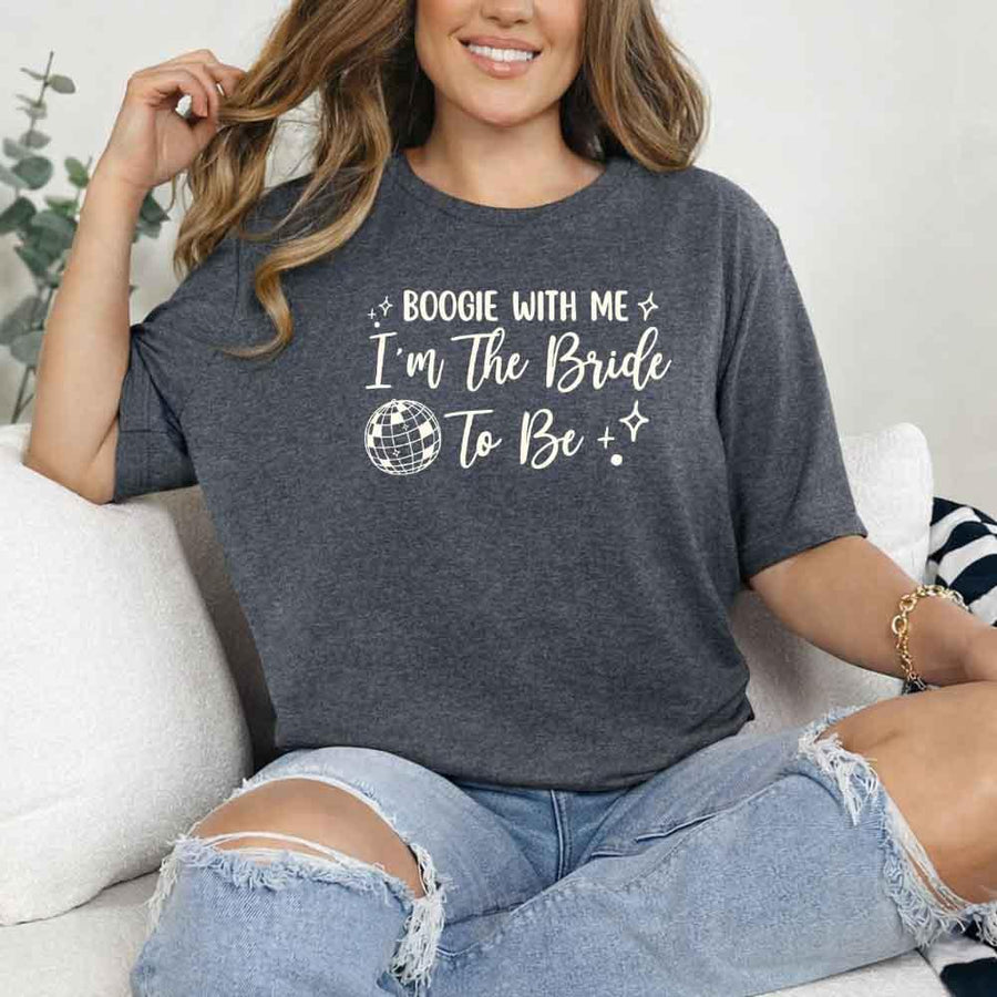 May include a Dark Heather retro-style graphic tee with bold disco lettering reading “Boogie With Me, I’m The Bride To Be,” featuring playful fonts and festive design elements!
