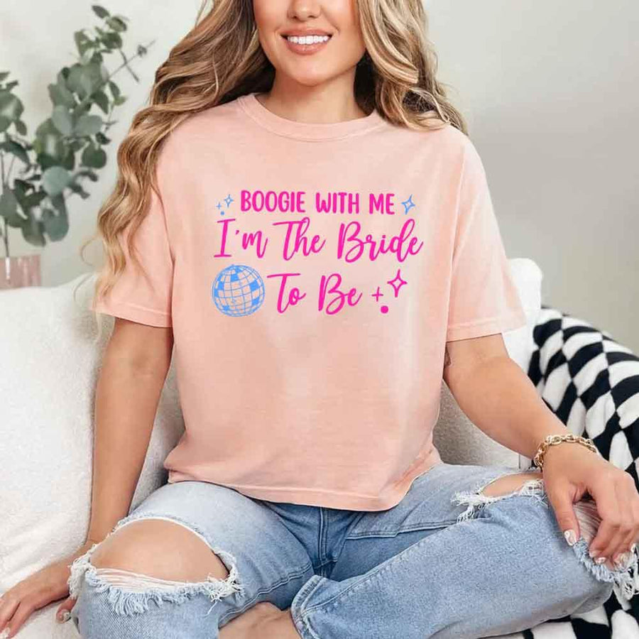 May include a Peach retro-style graphic tee with bold disco lettering reading “Boogie With Me, I’m The Bride To Be,” featuring playful fonts and festive design elements!