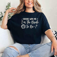 May include a Black retro-style graphic tee with bold disco lettering reading “Boogie With Me, I’m The Bride To Be,” featuring playful fonts and festive design elements!