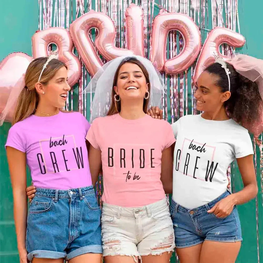 Three women wearing 'Bride to be' and 'Beach Crew' shirts with pink and silver balloons in the background.