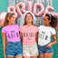 Three women wearing 'Bride to be' and 'Beach Crew' shirts with pink and silver balloons in the background.