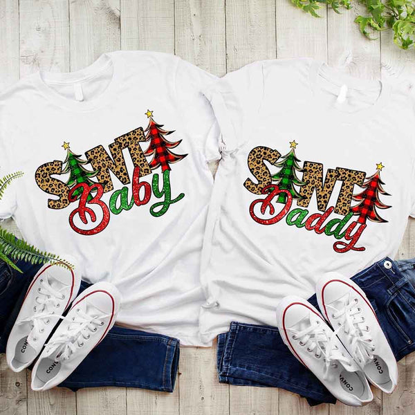 Two white t-shirts with 'Santa Baby' and 'Swt Daddy' text on a wooden surface with jeans and white sneakers.