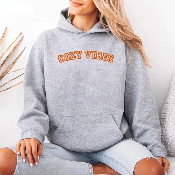 May include a unisex fall hoodie with “Cozy Vibes” text, featuring a soft fleece texture and autumn-inspired colors.