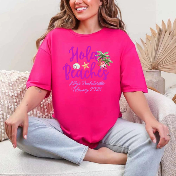 May include Heliconia bridesmaids wearing custom matching beach bachelorette T-shirts, relaxed seaside setting with sand and ocean backdrop, coordinated outfits, smiling and celebrating together outdoors!