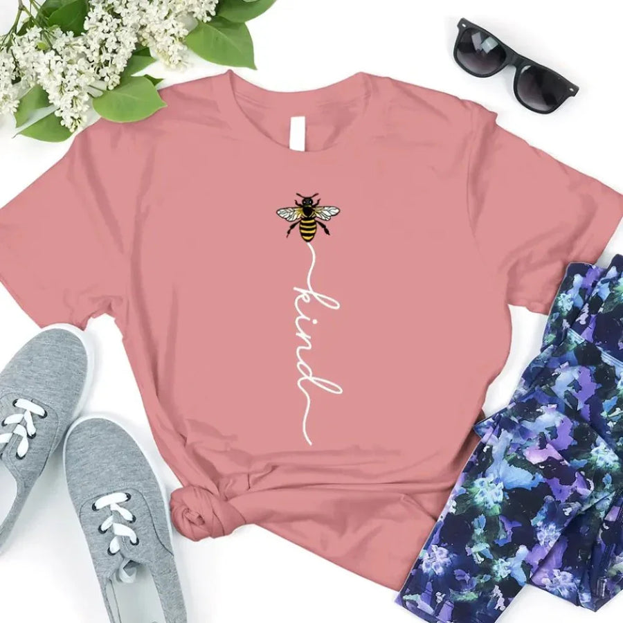 May include an inspirational t-shirt design featuring the phrase “Bee Kind” in flowing script lettering, often paired with a small bee graphic that adds a gentle, uplifting touch to the message.