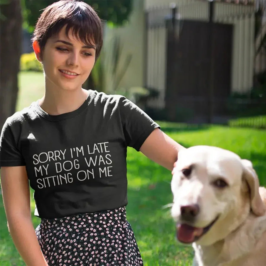 t-shirt with 'Sorry I'm late my dog was sitting on me' text, paired with jeans and sneakers on a wooden surface.