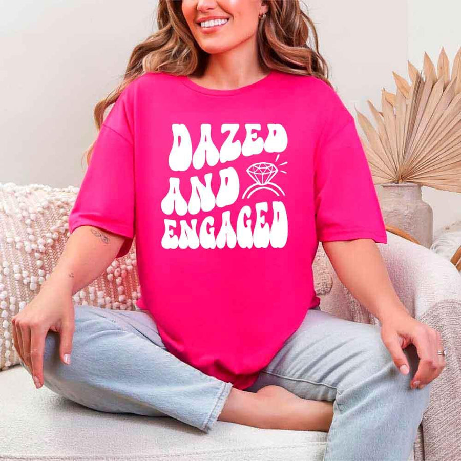 May include Heliconia group in colorful tie-dye shirts reading “Dazed & Engaged,” smiling at a bachelorette party, with bride in veil and fun, festive vibe!