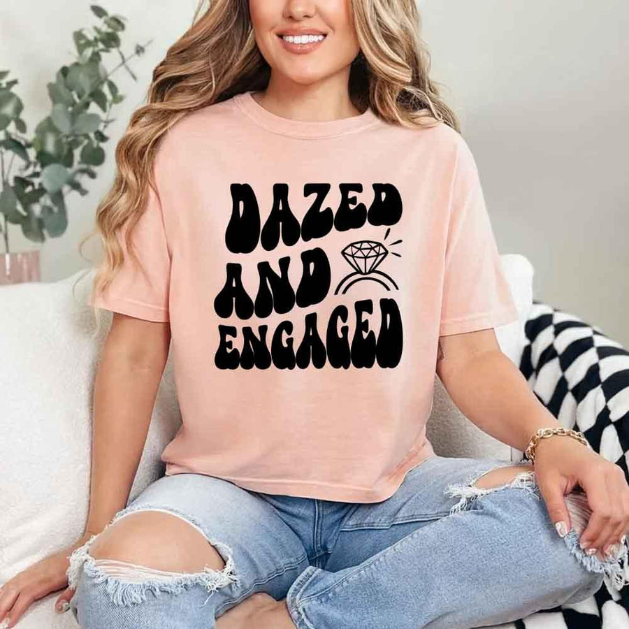 May include Peach group in colorful tie-dye shirts reading “Dazed & Engaged,” smiling at a bachelorette party, with bride in veil and fun, festive vibe!