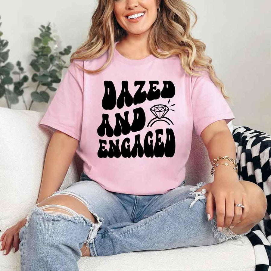 May include Pink group in colorful tie-dye shirts reading “Dazed & Engaged,” smiling at a bachelorette party, with bride in veil and fun, festive vibe!