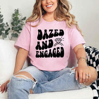 May include Pink group in colorful tie-dye shirts reading “Dazed & Engaged,” smiling at a bachelorette party, with bride in veil and fun, festive vibe!
