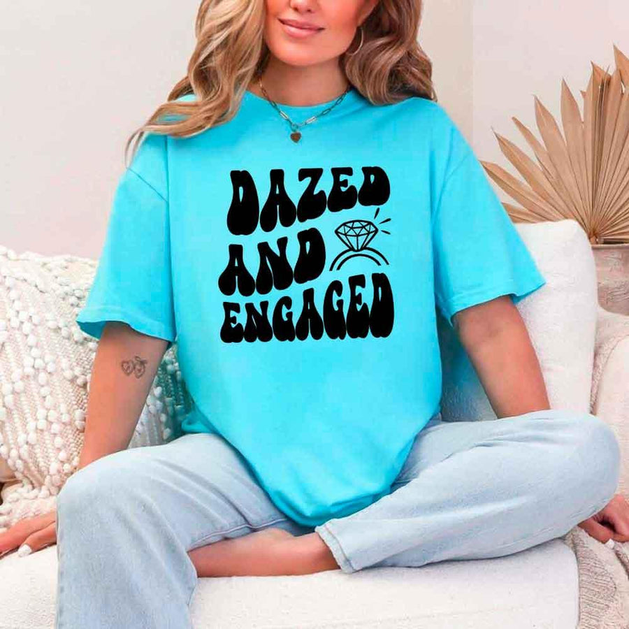 May include Turquoise group in colorful tie-dye shirts reading “Dazed & Engaged,” smiling at a bachelorette party, with bride in veil and fun, festive vibe!