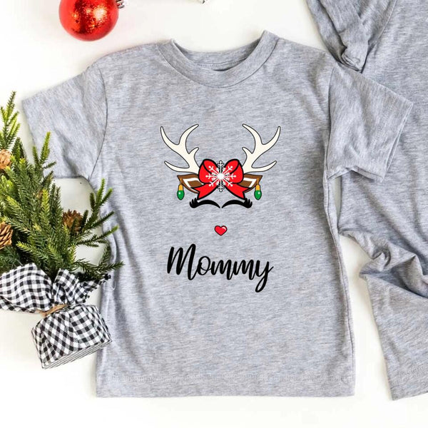 Folded red or white unisex Christmas T-shirt with a simple reindeer graphic design, styled beside ornaments and pine décor for a cozy holiday look.