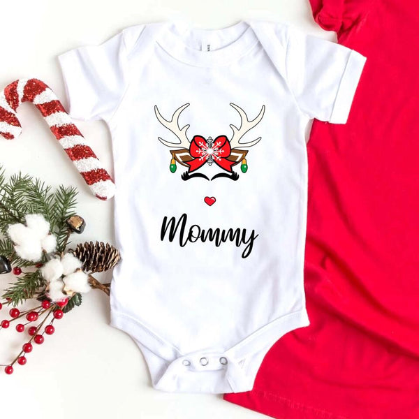 Folded red or white unisex Christmas T-shirt with a simple reindeer graphic design, styled beside ornaments and pine décor for a cozy holiday look.