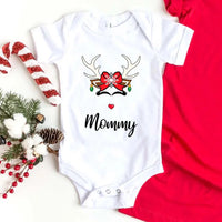 Folded red or white unisex Christmas T-shirt with a simple reindeer graphic design, styled beside ornaments and pine décor for a cozy holiday look.